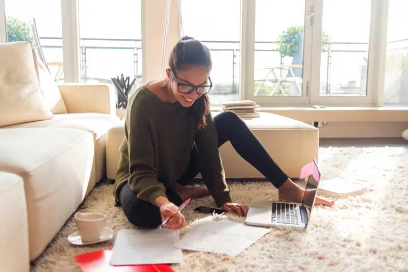 Woman sitting on the floor, reviewing documents and filing her taxes, focusing on unemployed taxes and maximizing her tax refund.