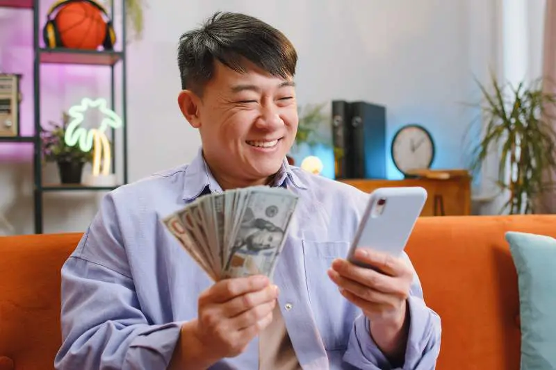 Man smiling at his phone while holding money, excited about the possibility of filing taxes for free with easy federal tax filing options
