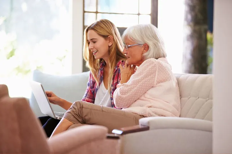 A woman guiding her mother through tax preparation on a laptop, illustrating support in filing taxes for someone else.