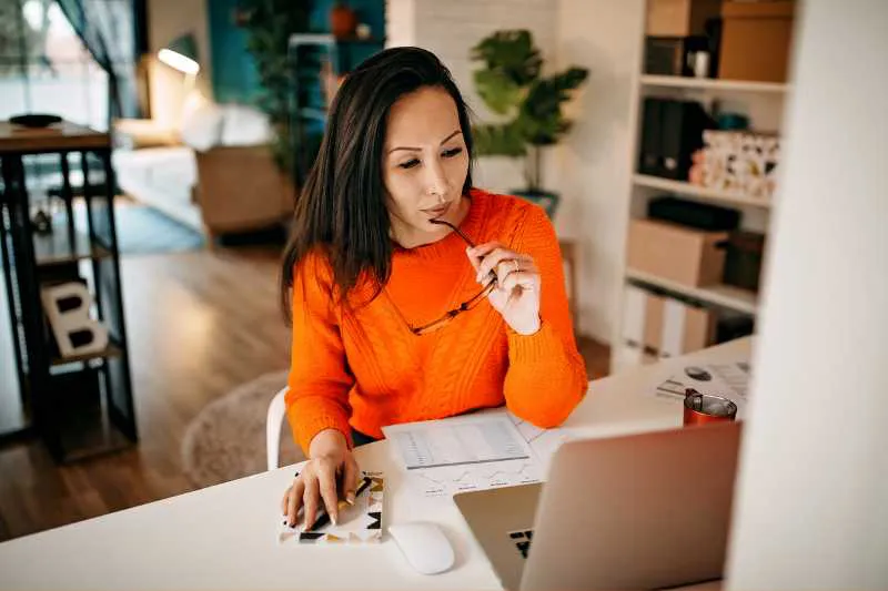 Woman wondering whether she needs to file taxes, looking at her laptop and paperwork.