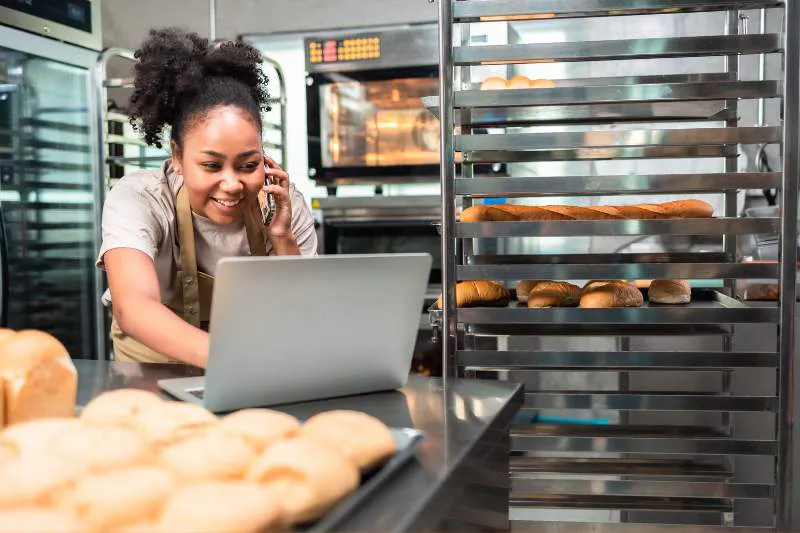 Woman managing her sole proprietorship taxes and business finances on a laptop in a bakery, following tax tips for self-employed workers.