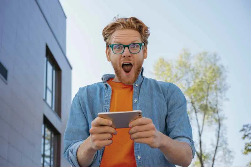 Man excitedly checking his phone, surprised by the valuable tax breaks and savings he discovered for his upcoming tax filing.